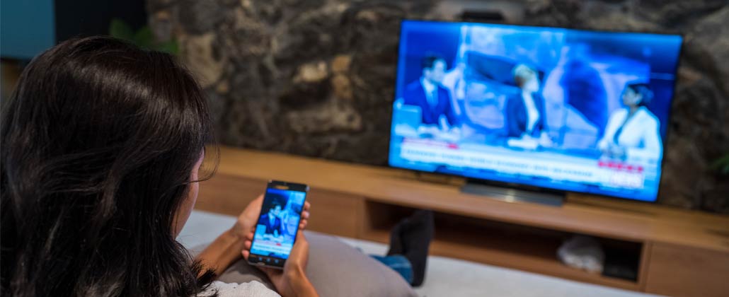 Mulher com telemóvel na mão e a ver televisão